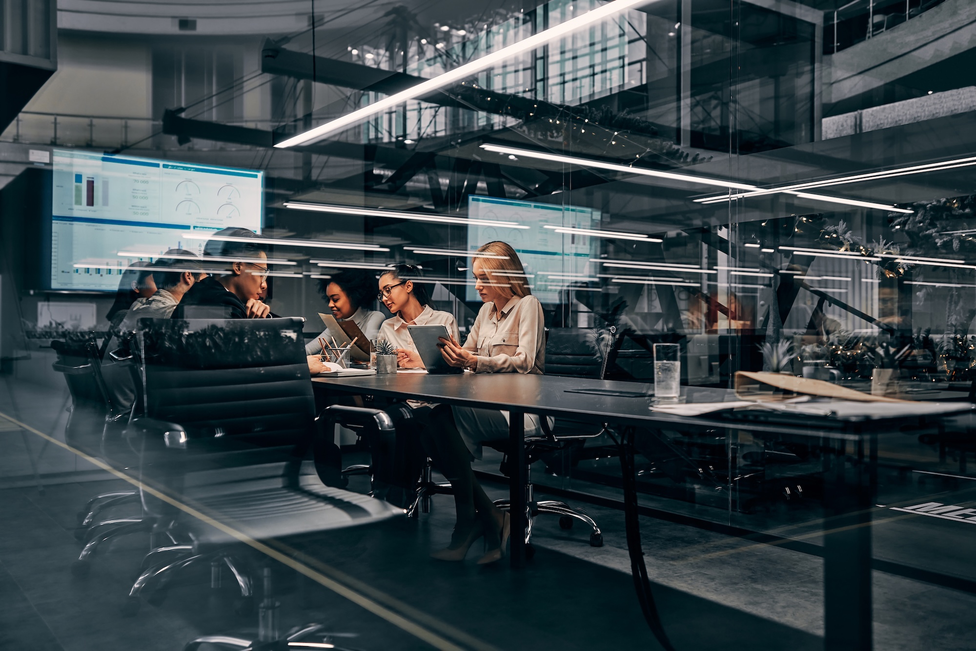 Modern Busy Office Environment Modern business. Young focused serious business women and men working in a conference room working on a project presentation. Light from a spacious office is reflected through the glass.